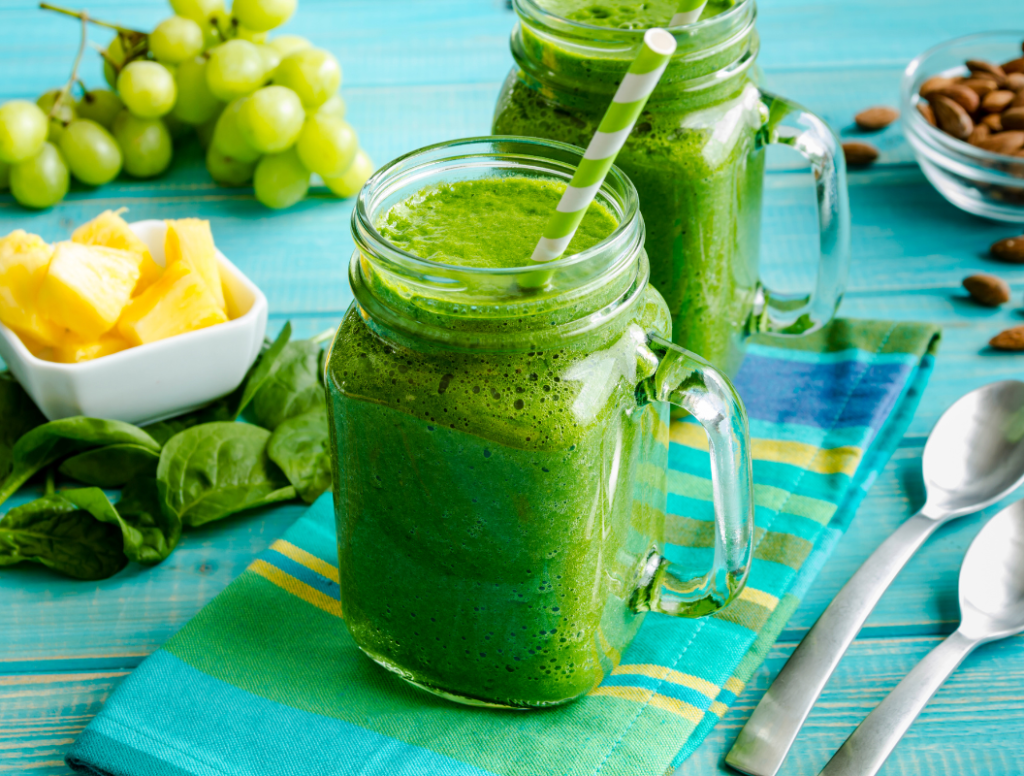 Two mason jars of green smoothie recipes with grapes, pineapple, spinach, and almonds.